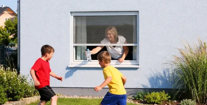Kinder spielen vor einem Fenster mit Fliegengitter Rollo