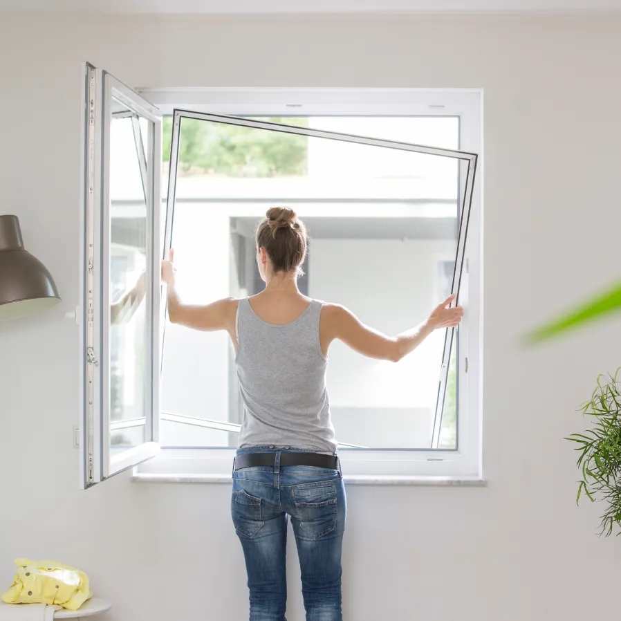 Frau öffnet Fenster mit Fliegengitter Spannrahmen als Insektenschutz nach Maß