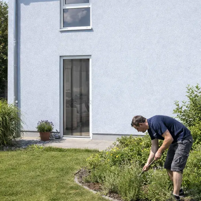 Mann arbeitet im Garten vor einer Tür mit Insektenschutz